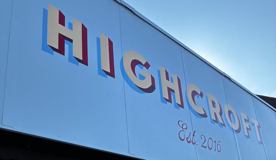 The exterior of a storefront with a large light blue sign reading 'HIGHCROFT Est. 2016' in raised multicolored letters.